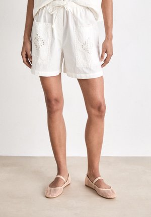 White cotton shorts featuring embroidered side pockets with a decorative lace trim. Paired with light pink mesh ballet flats.