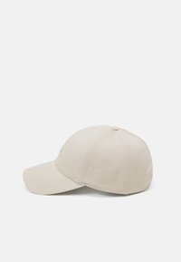 Beige baseballcap med mykt stoff, buet skjerm og sømmer. Har en logo i kontrastfarge på frontpanelet.