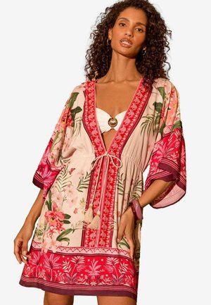 Floral kaftan dalam warna merah muda terang dengan hiasan merah cerah. Memiliki kerah v yang dalam, lengan pendek, dan pinggang dengan tali serut serta hiasan tassel.