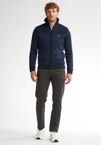 Marinegebreid zip-up vest met een gestructureerd bovenstuk, gecombineerd met donkere broek en lichte sneakers. Heeft zijzakken en een merkembleem.