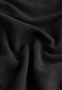 Tissu noir avec des plis souples et une texture fine tricotée créant des ombres et des reflets doux.
