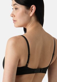 Reggiseno nero con sottili spalline regolabili, tessuto testurizzato e chiusura posteriore a più ganci. Design semplice che si concentra sulla funzionalità.