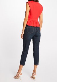 Röd peplumtopp med figursydd midja och axeldetaljer, tillsammans med mörkblå korta jeans och vita sandaletter med remmar.
