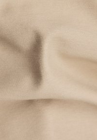 Béžová texturovaná látka, mírně pomačkaná, ukazující hladké tkaní s jemnými detaily, vhodná pro různé textilní aplikace.