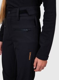 Közelkép egy személyről, aki fekete softshell nadrágot visel cipzáras zsebbel és narancssárga "Brunotti" logóval a combján, fekete fleece dzsekivel párosítva.
