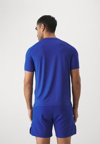 Camisa deportiva azul de manga corta, hecha de una tela suave. Presenta un cuello redondo y un ajuste ceñido, combinada con pantalones cortos a juego.