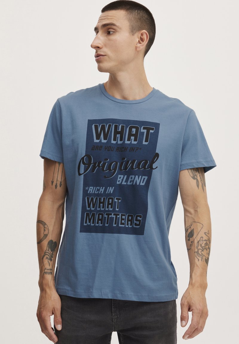 Blå bomulds T-shirt med fed sort tekst med sætninger som "HVAD" og "Original Blend." Korte ærmer og rund halsudskæring.