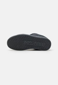 Black sneaker outsole with textured grip pattern. Features a molded logo in the center. Durable rubber material, designed for traction.