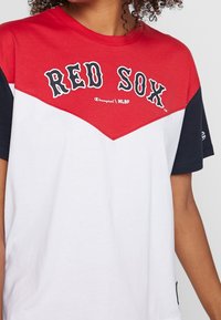 Camiseta corta de manga corta en rojo y blanco con detalles en azul, que presenta el logo "RED SOX" en negro. Fabricada en algodón, con cuello redondo y corte relajado.