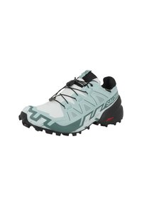 Lichtgroene en witte trailrunschoen met een gestructureerd bovenwerk, schuine vormgeving, zwarte veters en een robuuste zwarte zool met noppen.