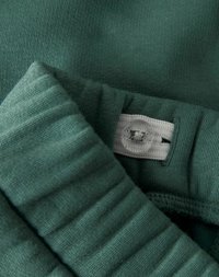 Zielona dzianina z żebrowanym brzegiem i regulowaną białą elastyczną taśmą z przezroczystym guzikiem do dopasowania rozmiaru.