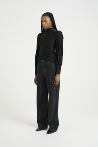 Svart langermet topp med puffede skuldre og dekorative hvite knapper. Høyt midje mørke jeans med en glitrende tekstur og vid ben.