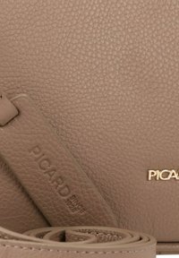Bolso de cuero marrón texturizado con un logo dorado, que presenta una correa suave y un sutil detalle en relieve del nombre de la marca.