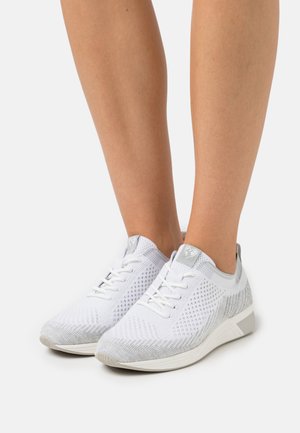 Baskets blanches avec une tige en tricot texturé, accents gris, et lacets blancs. Elles présentent un design épuré et un léger talon.
