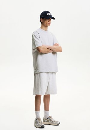T-shirt en coton gris et shorts assortis, tous deux amples. Les accessoires comprennent une casquette noire avec le texte "Oregon" et des baskets gris clair.