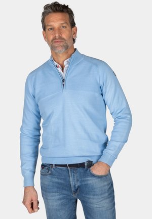 Lichtblauwe zip-up sweater met ribbeltextuur op de schouder, lange mouwen en een rechte zoom. Gecombineerd met blauwe denim jeans en een zwarte riem.