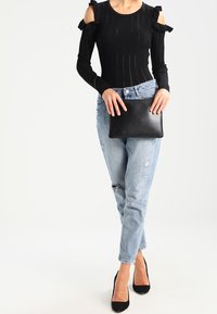 Zwarte geribbelde longsleeve top met geschulpte schouderdetails; lichtblauwe distressed jeans; houdt een zwarte leren clutch vast; draagt zwarte hoge hakken.