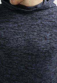 Hoodie i marinblått med en texturerad, mönstrad tyg. Har en subtil blandning av mörka och ljusa nyanser, med en tight passform.