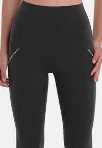 Zwarte leggings met een hoge tailleband, een gladde textuur en zijzakken met witte accenten. Ontworpen voor comfort en flexibiliteit.