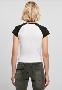 T-skjorte med kort erm og hvit kropp samt svarte raglan-ermer, laget av mykt stoff. Kombinert med mørk grå jeans med baklommer.