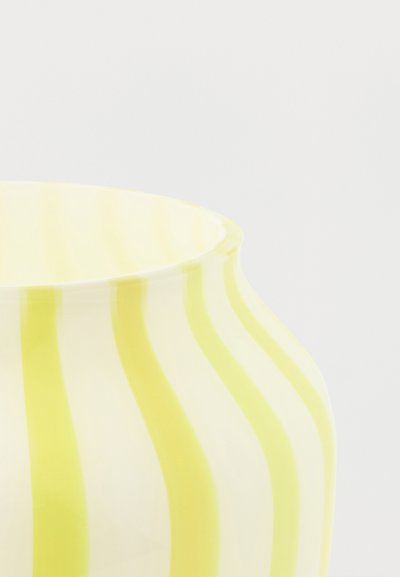 Gros plan sur un vase rayé jaune et blanc avec un corps large et arrondi et un bord légèrement évasé sur un fond uni.