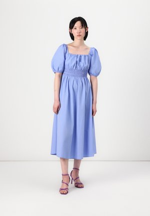 Abito azzurro chiaro fino al ginocchio con maniche a sbuffo e corpino smock. Abbinato a tacchi a strappo viola. Tessuto semplice e liscio.