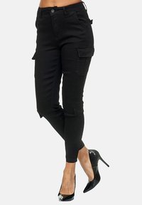 Schwarze Cargo-Hosen im Slim-Fit mit Seitentaschen und glatter Textur. Kombiniert mit schwarzen High-Heels.
