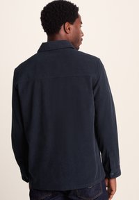 Navy corduroy shirt with a button-up front, collar, and long sleeves. Textured fabric with a slightly relaxed fit, visible stitching detail.