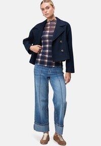Két soros, rövid navy peacoat, kockás blúz, világoskék, bő szárú farmernadrág, kontrasztöltésekkel, és barna fűzős sportcipő.