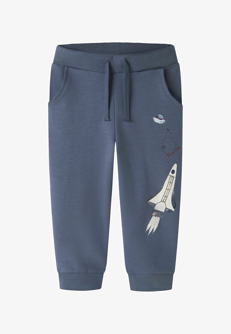 Pantalones deportivos infantiles azules con bolsillos frontales, cintura con cordón y un gráfico temático espacial de nave cohete y OVNI en la pierna derecha.