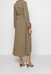 Abito midi floreale marrone con maniche lunghe, vita aderente e gonna fluida. Abbinato a sandali con tacco a spillo e cinturino.