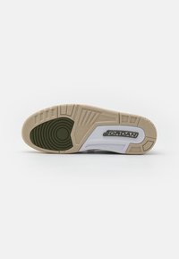 Semelle d'une basket Jordan beige et blanche avec un motif de grip circulaire noir et le logo "JORDAN" sur la partie médiane du pied.
