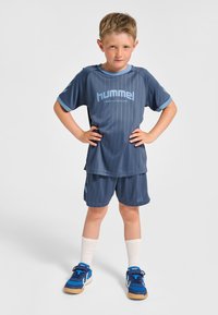 Blaues Sportoutfit mit vertikalen Streifen, kurzärmeliges Shirt und Shorts, kombiniert mit blauen Turnschuhen und weißen Socken. Auffälliges Logo sichtbar.