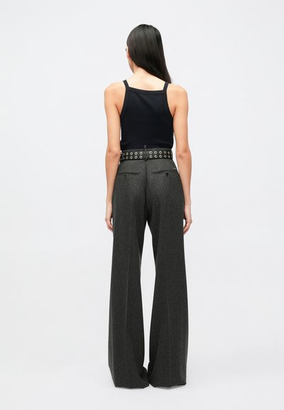 Black tank top with thin straps, paired with wide-leg, textured gray pinstripe trousers. Belt features metal eyelets and back pockets.