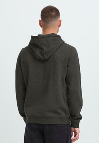 Man with short hair wearing a dark gray hoodie and black pants, viewed from behind against a plain light background.