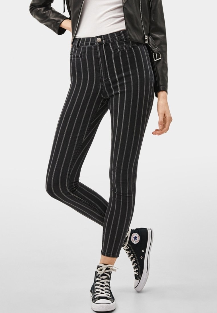 Černé a šedé pruhované džíny s vysokým pasem, úzkým střihem a elastickým materiálem, doplněné černými vysokými teniskami.