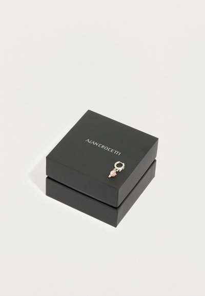 Melna Alan Crocetti rotaslietu kārbiņa ar vienu sudraba stīpas auskaru, kuram augšpusē ir neliela rozā sirds formas piekariņš.