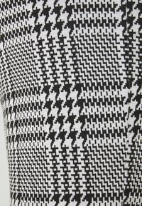 Pattern di tessuto houndstooth in bianco e nero con forme frastagliate interconnesse che creano un design geometrico testurizzato.