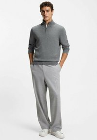 Pull gris à col zippé avec manches longues assorti à un pantalon gris clair. La tenue présente une coupe décontractée et un tissu doux sans motifs visibles.