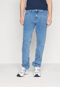 Ljust blå denimjeans med rak passform, femfickorsdesign och bälteshällor, kombinerat med vita träningsskor.