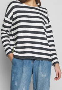 Randig långärmad tröja i svart och vitt, lätt stickad kvalitet med en avslappnad passform. Har en sidodetalj i livlig grön.