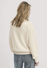 Helle, ribbed Sweater mit lässiger Passform, langen Ärmeln und weitem Ausschnitt, kombiniert mit hellblauen Denim-Jeans.