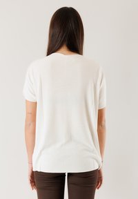 Top in maglia bianco, a maniche corte, con vestibilità comoda, caratterizzato da un colletto rotondo e orlo a coste. Il tessuto ha una consistenza morbida e liscia.