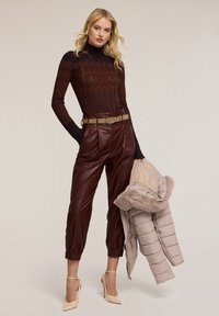 Maglione lavorato a maglia bordeaux con motivo a zigzag, collo alto, pantaloni in similpelle bordeaux con cintura e giacca trapuntata beige con rifiniture in pelliccia.