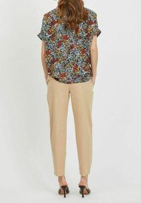 Mustikka kukkapaidan musta väri punaisilla, sinisillä ja keltaisilla yksityiskohdilla; vaaleanruskeat kapenevat housut; korkokengät; lyhyet hihat; rento malli.