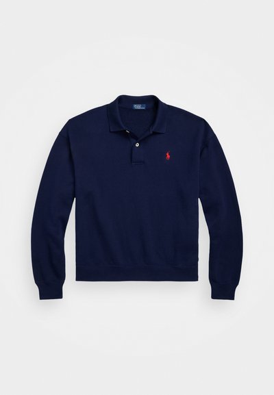Tums zils garām piedurknēm polo krekls, kas izgatavots no kokvilnas, ar divu pogu aizdari, ribota piedurkņu maliņu un sarkanu izšūtu logotipu uz krūtīm.