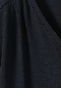Gros plan d’un tissu bleu marine foncé avec une couture en V et un détail subtilement froncé sur le côté supérieur gauche du vêtement.