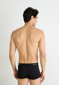 Zwarte katoenen boxershorts met een logo op de tailleband, met een gladde textuur en een fitted ontwerp. Model staat van achteren, toont de achterkant.
