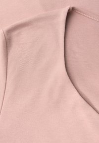 Ljust rosa tyg med en slät textur och rundad halsringning. Materialet verkar elastiskt och mjukt, och har en minimalistisk design.