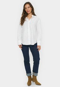 White shirt with light blue heart patterns, button front, long sleeves, paired with dark denim, rolled cuffs, and brown ankle boots.